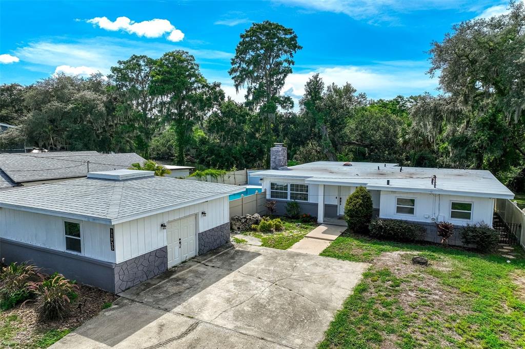 A white house with a detached garage and a concrete driveway sits among mature trees — 11935 RIVERHILLS DRIVE, TAMPA, FL