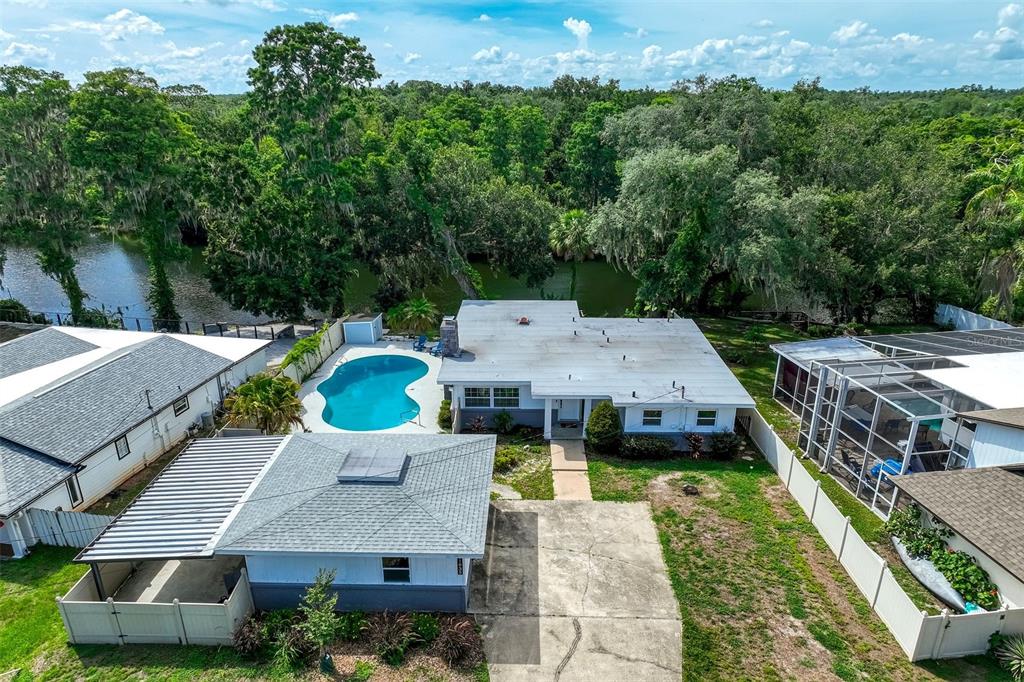 An aerial view shows a house with a pool, a detached garage, and a waterfront backyard — 11935 RIVERHILLS DRIVE, TAMPA, FL