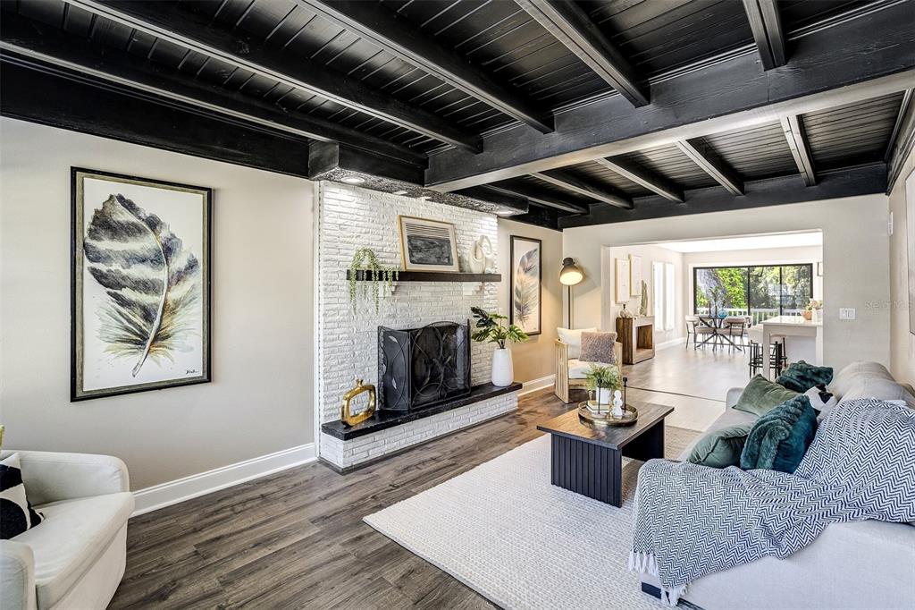 A living room features a white brick fireplace, dark wood-beamed ceiling, and wood-look flooring — 11935 RIVERHILLS DRIVE, TAMPA, FL