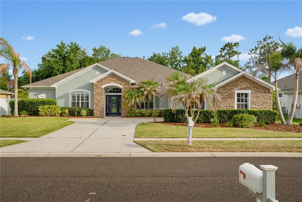 A single-story house with a stone facade, a concrete driveway, and palm trees in front — 11704 NEWBERRY GROVE LOOP, RIVERVIEW, FL