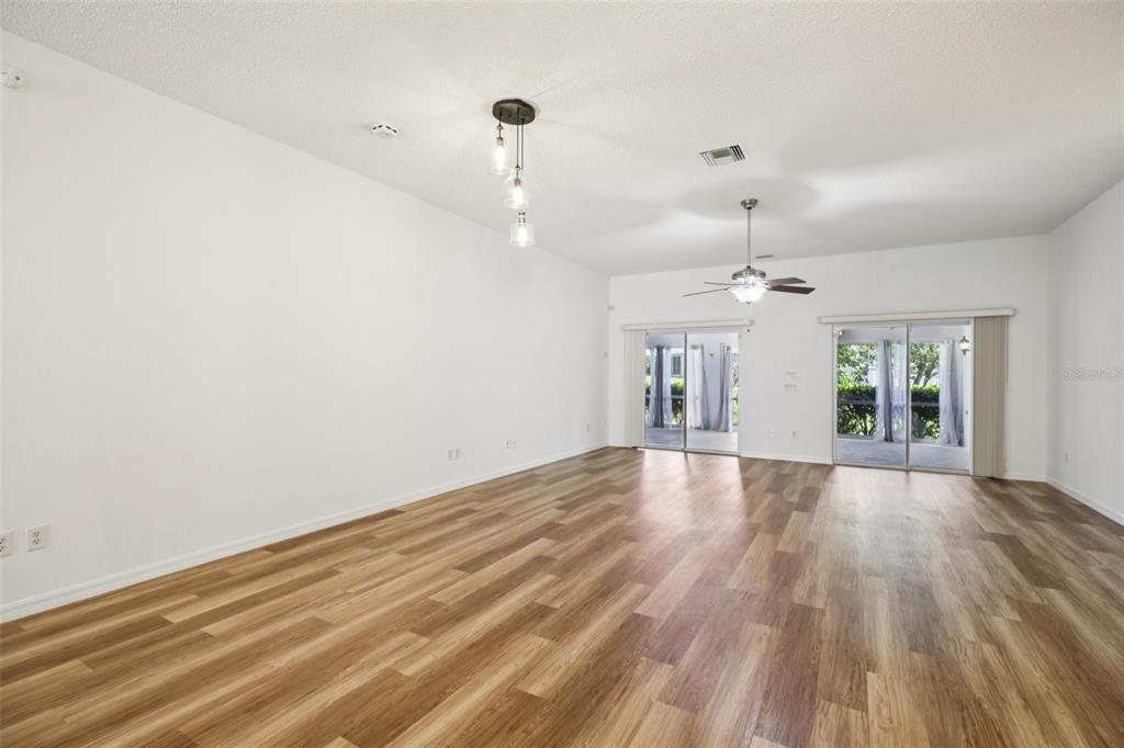 A spacious living room features wood-look flooring, white walls, a ceiling fan, and sliding doors — 8690 SE 173RD WISTERIA STREET, THE VILLAGES, FL
