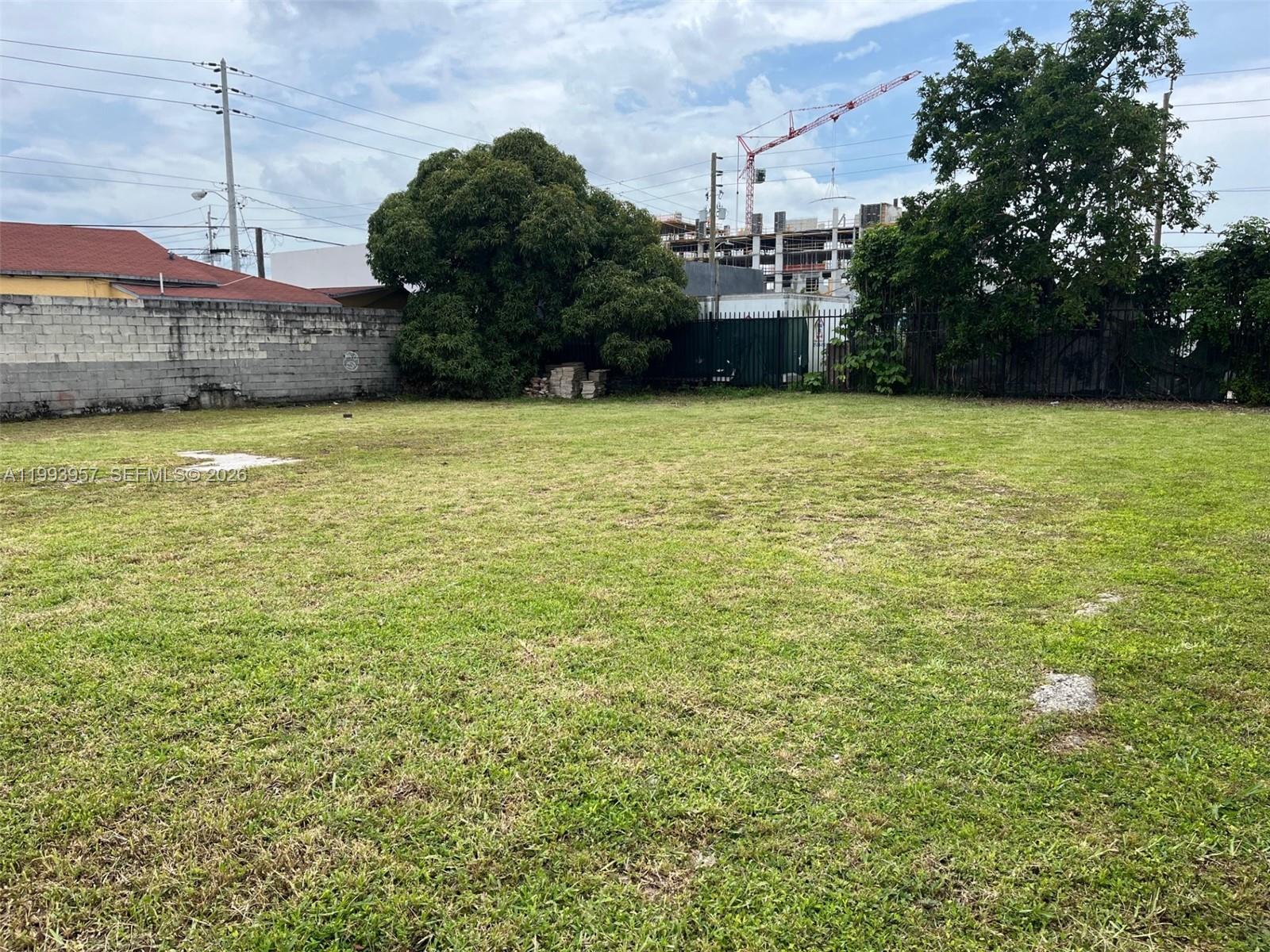 A large, flat, grassy vacant lot is enclosed by a concrete wall and metal fencing — 2410 NW 7th Ct, Miami FL 33127, MIAMI, FL