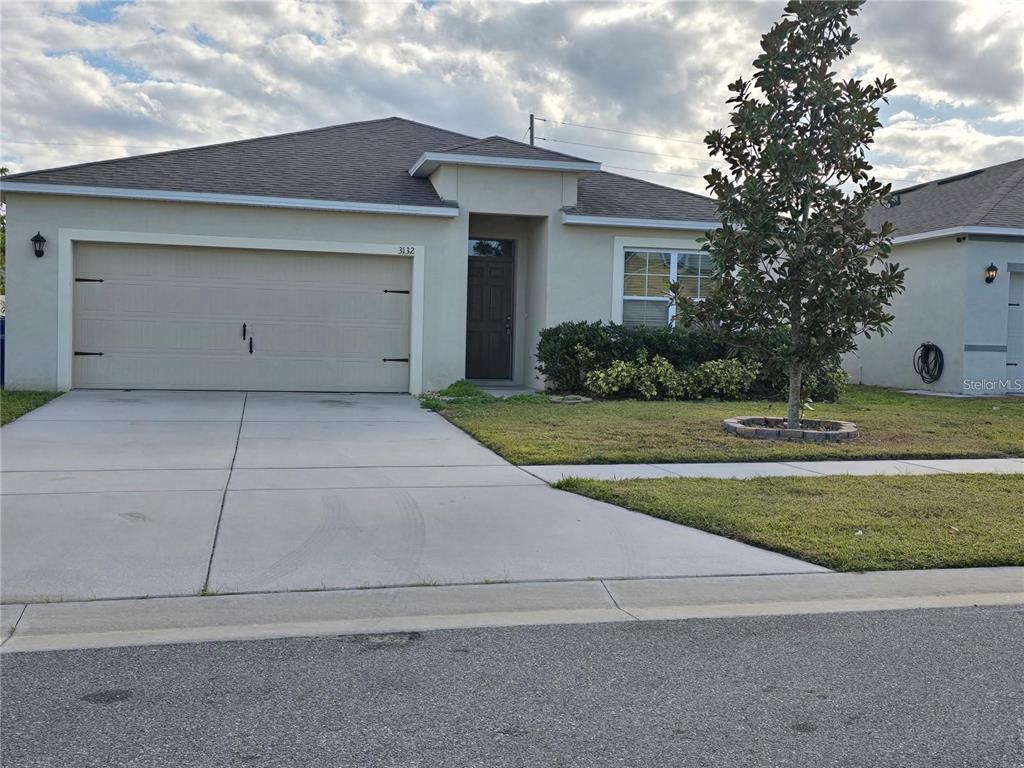 A single-story house with a beige stucco exterior, a two-car garage, and a front lawn — 3132 COUNTRY CLUB CIRCLE, WINTER HAVEN, FL