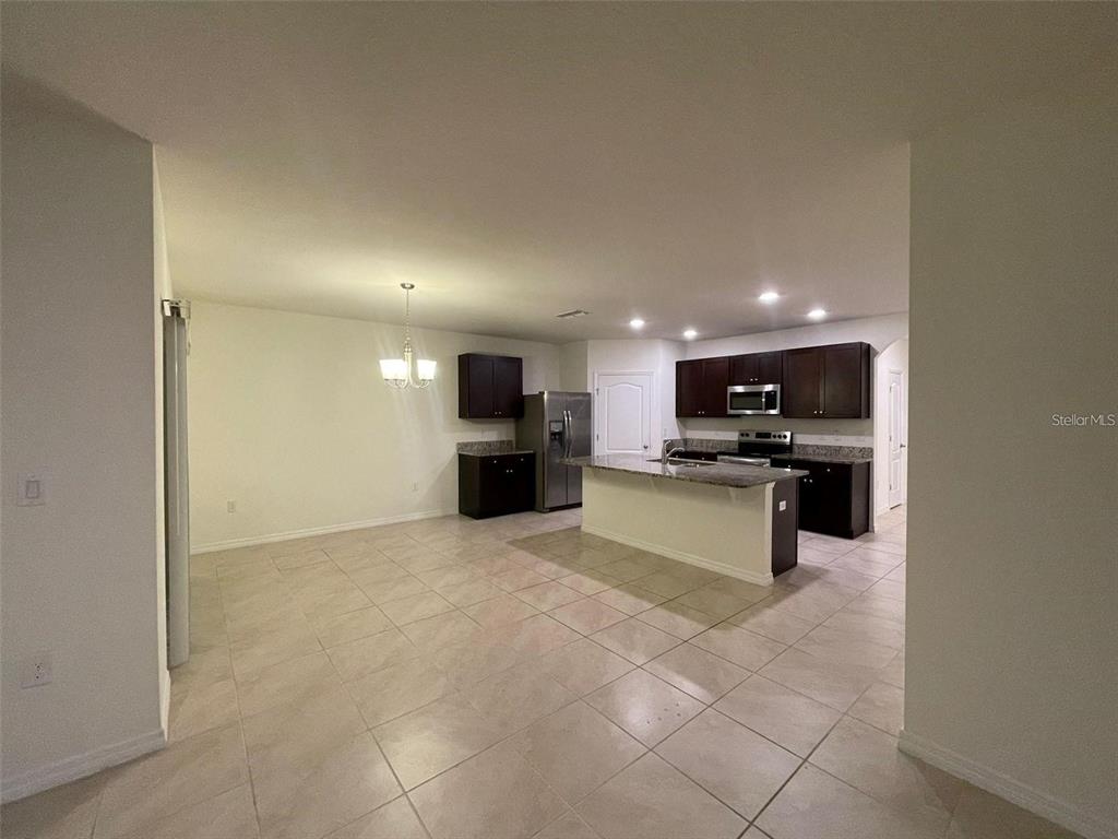 An open-concept kitchen features dark wood cabinets, granite countertops, and light-colored tile flooring — 3132 COUNTRY CLUB CIRCLE, WINTER HAVEN, FL