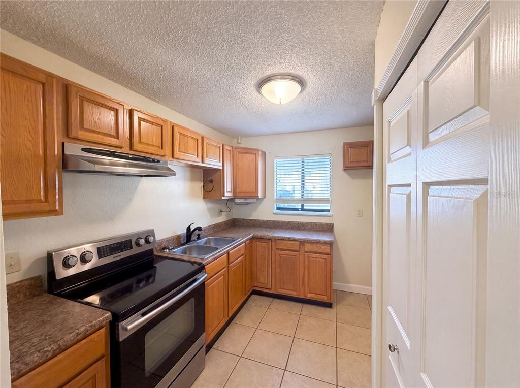 A kitchen features wood cabinets, laminate countertops, a stainless steel range, and tiled flooring — 22707 WATERSEDGE BOULEVARD UNIT 53, LAND O LAKES, FL