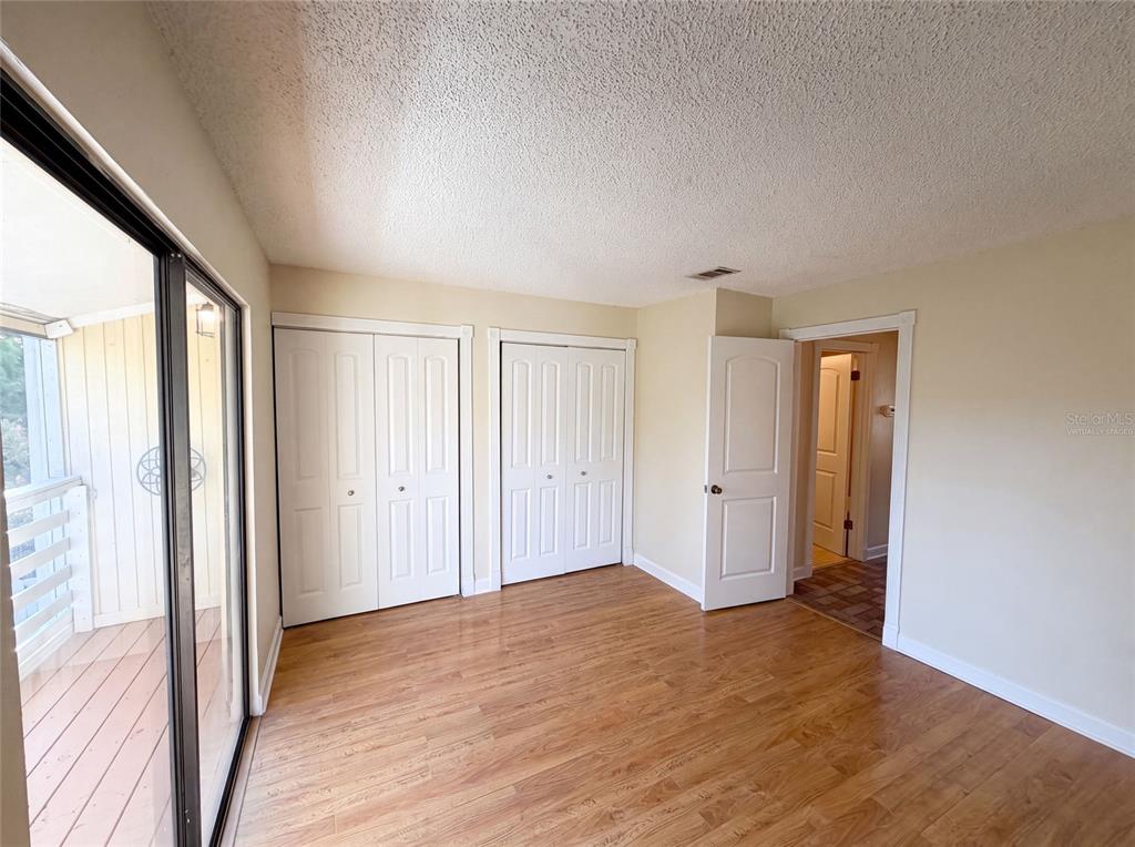 An empty bedroom features wood-look flooring, two sets of closet doors, and a sliding glass door — 22707 WATERSEDGE BOULEVARD UNIT 53, LAND O LAKES, FL