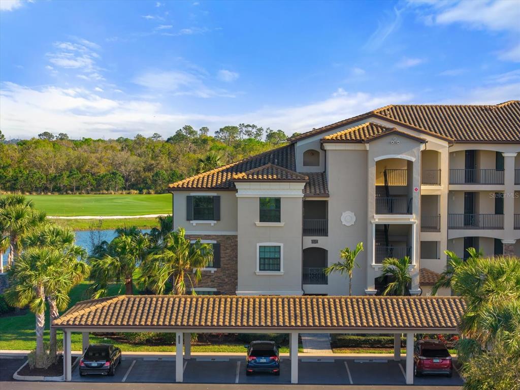 An exterior view of a multi-story apartment building with a covered parking area in front — 16904 VARDON TERRACE UNIT 301, LAKEWOOD RANCH, FL