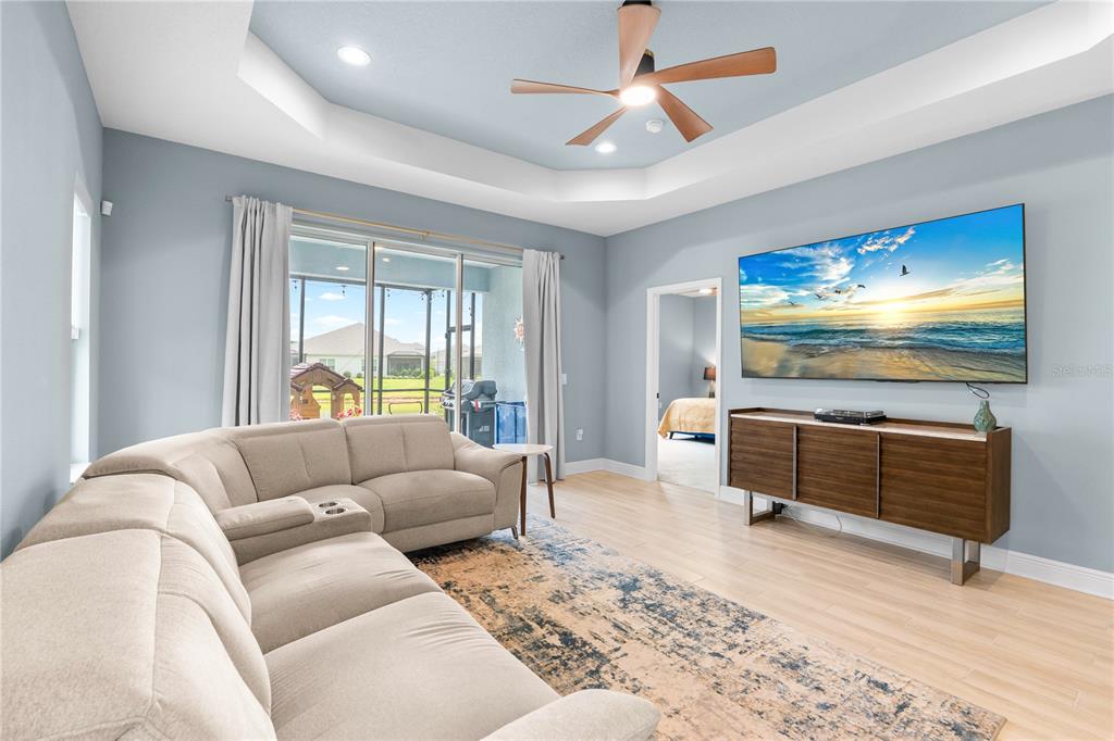 A living room features a sectional sofa, a wall-mounted television, and a tray ceiling — 9950 CROSS RIVER TRAIL, PARRISH, FL