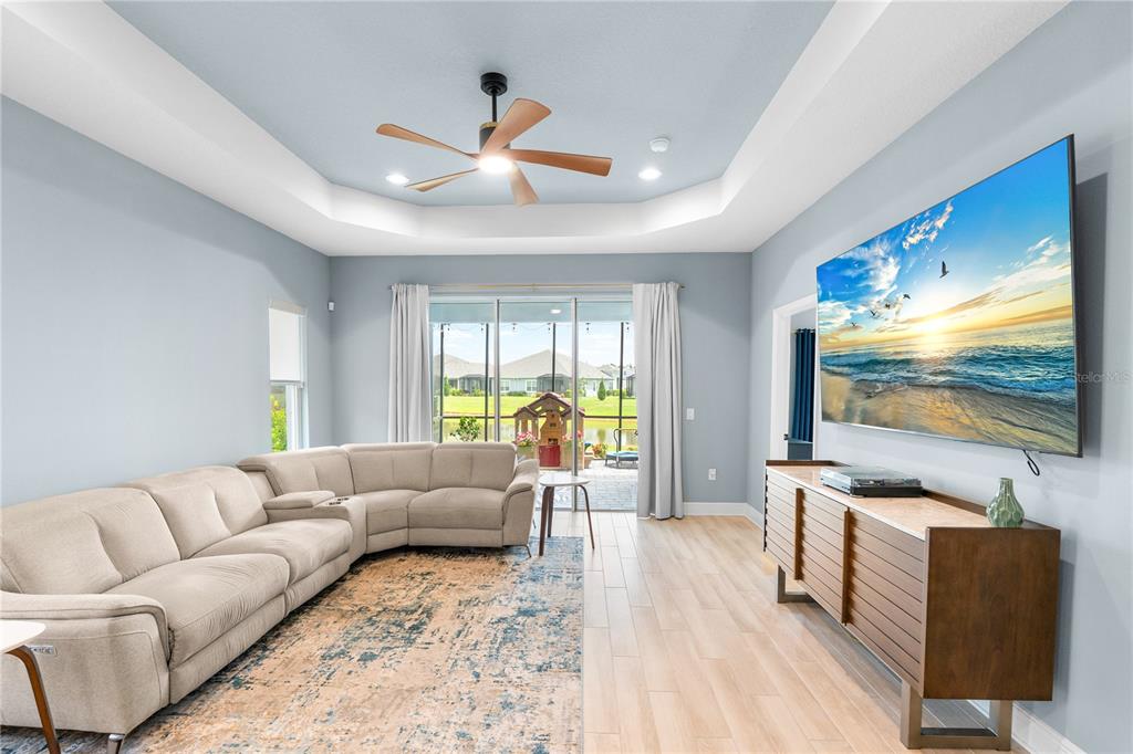 A living room features a beige sectional sofa, a large wall-mounted television, and a tray ceiling — 9950 CROSS RIVER TRAIL, PARRISH, FL