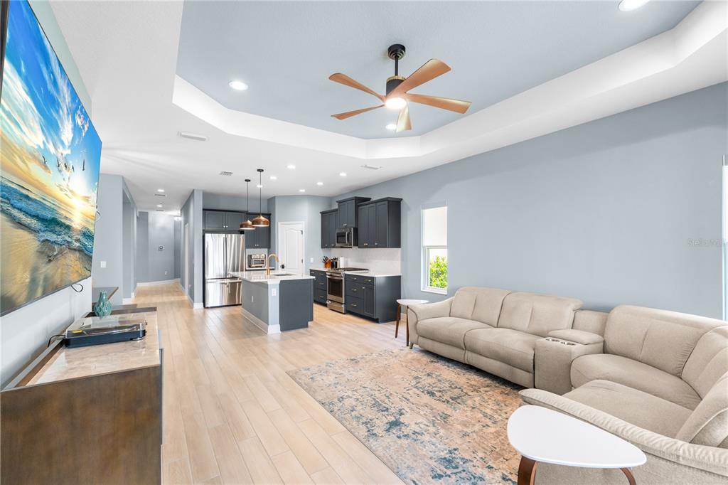 An open-concept living room and kitchen feature light wood-look flooring and dark gray cabinetry — 9950 CROSS RIVER TRAIL, PARRISH, FL