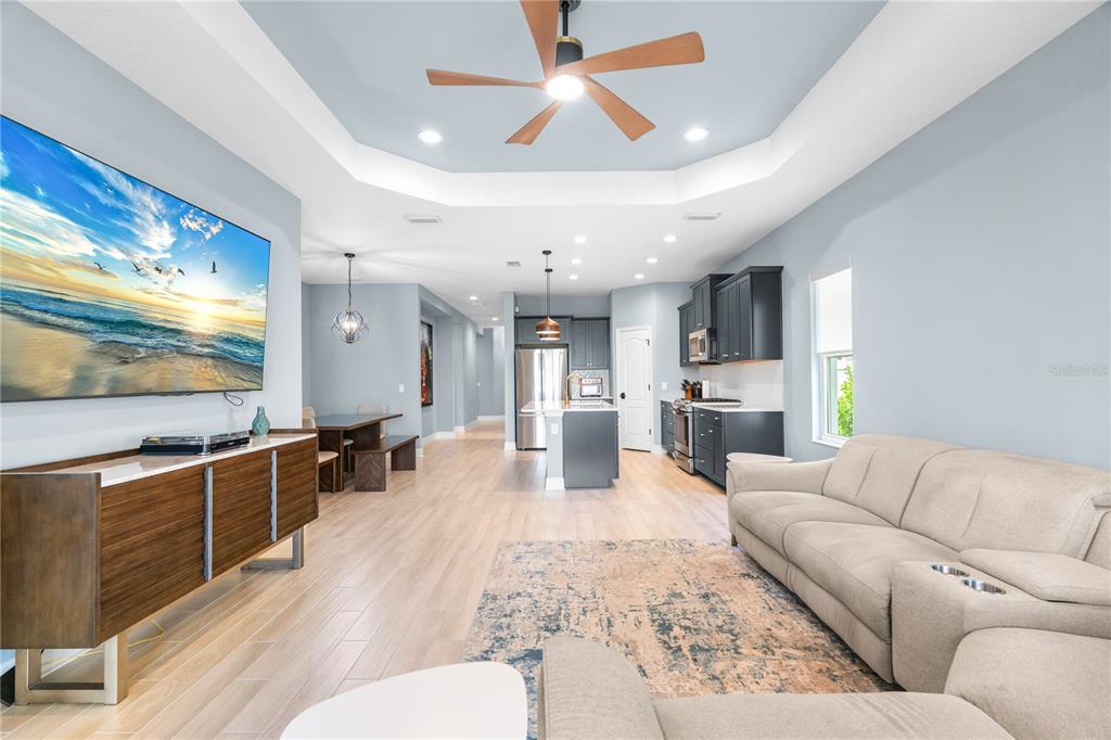 An open-concept living room and kitchen feature light wood floors, a tray ceiling, and cabinetry — 9950 CROSS RIVER TRAIL, PARRISH, FL
