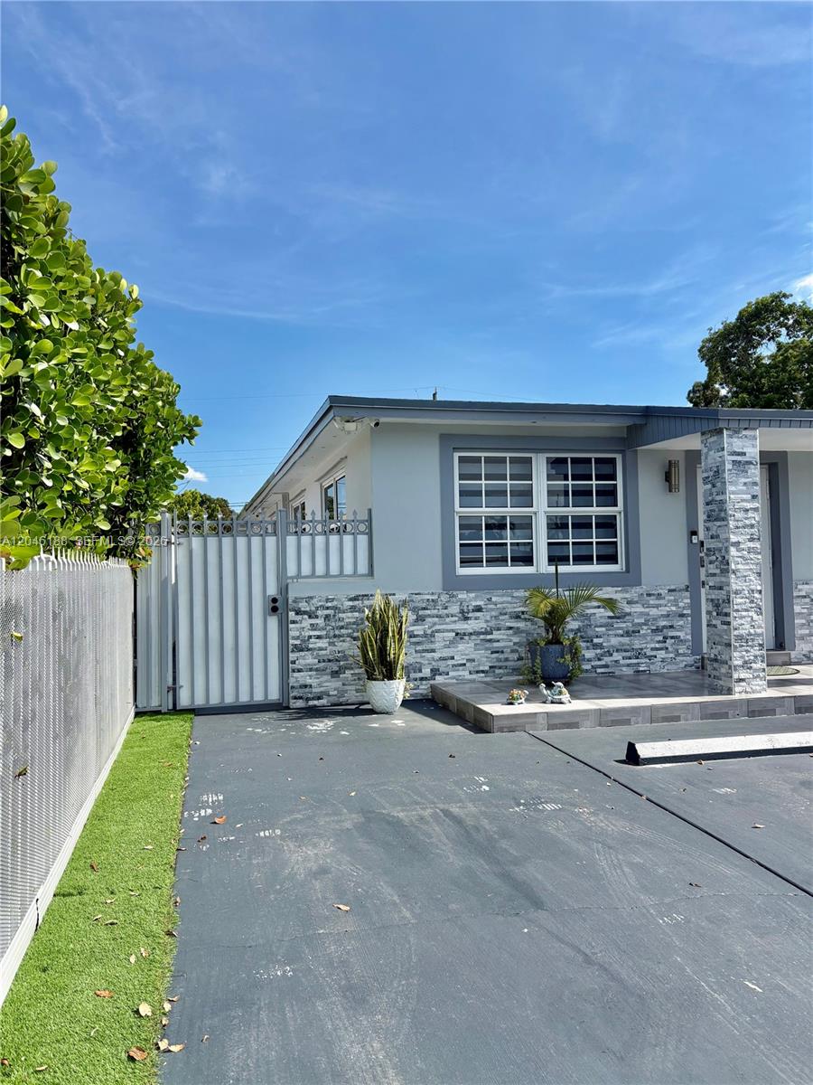 A gray house exterior features a paved driveway, a white gate, and stone-tiled accents — 734 E 39th St, Hialeah FL 33013, HIALEAH, FL