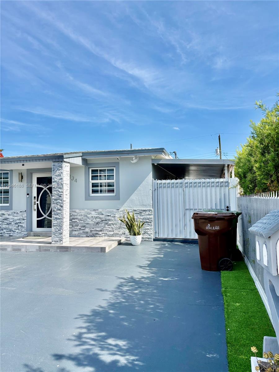 A single-story house exterior features a gray driveway, stone-veneer accents, and a white metal gate — 734 E 39th St, Hialeah FL 33013, HIALEAH, FL