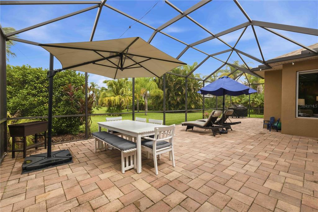 A screened-in patio features a dining set, lounge chairs, and a blue umbrella — 5723 114TH DRIVE E, PARRISH, FL