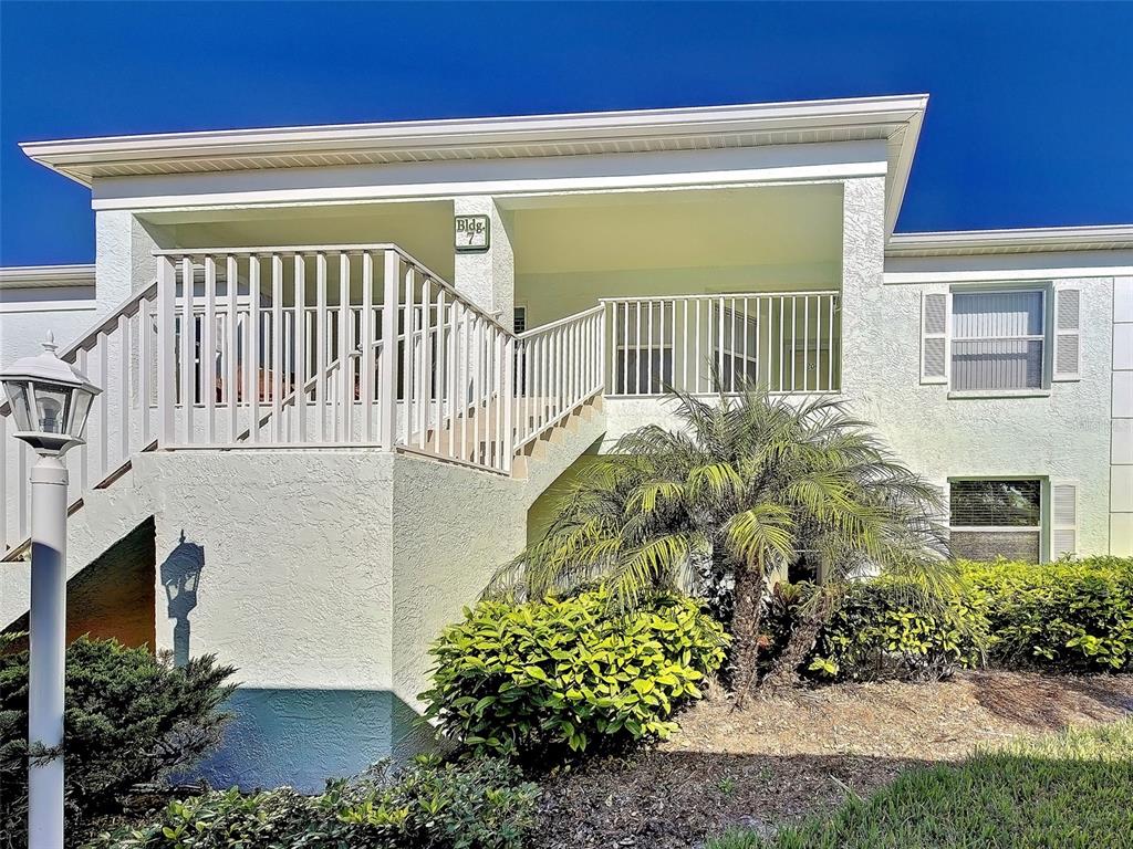An exterior view of a two-story apartment building with a staircase and a palm tree — 5725 GREENWOOD AVENUE UNIT 7104, NORTH PORT, FL