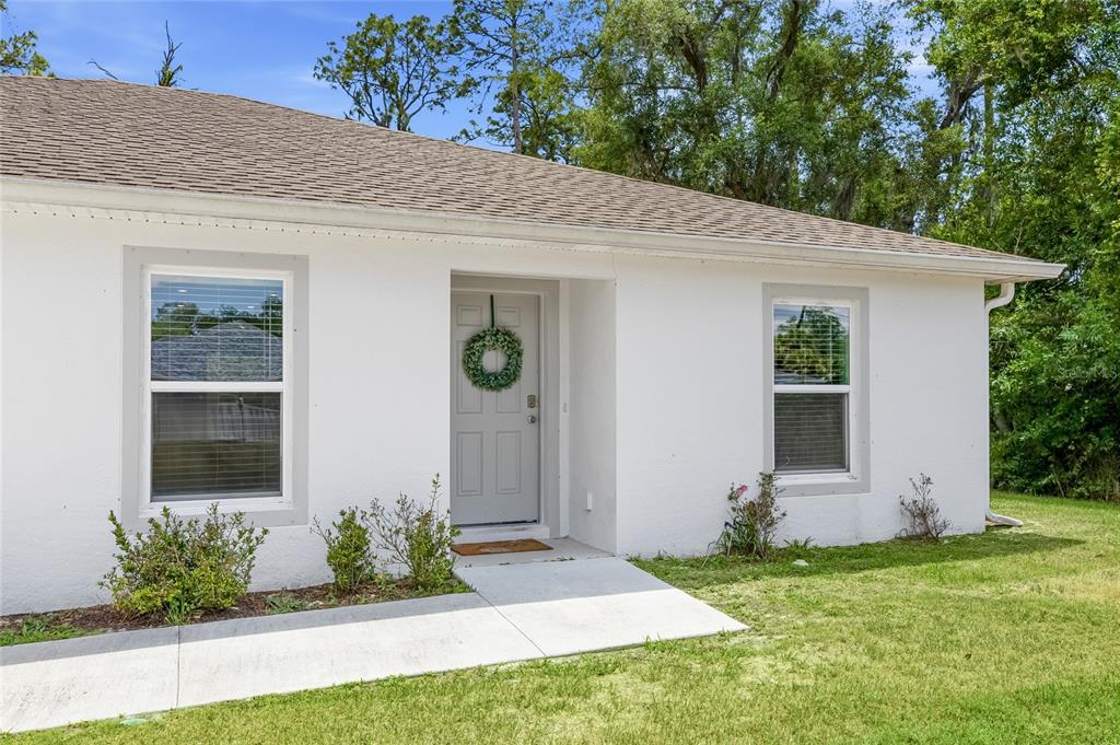 A white house exterior features a gray front door with a wreath and two windows — 3618 WHITMAN STREET, NORTH PORT, FL