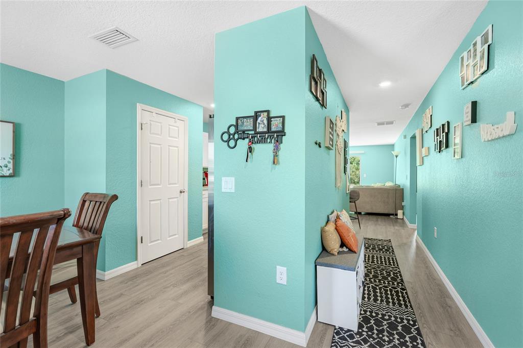 A turquoise-walled hallway leads to a living area with light wood-look flooring and decor — 3618 WHITMAN STREET, NORTH PORT, FL