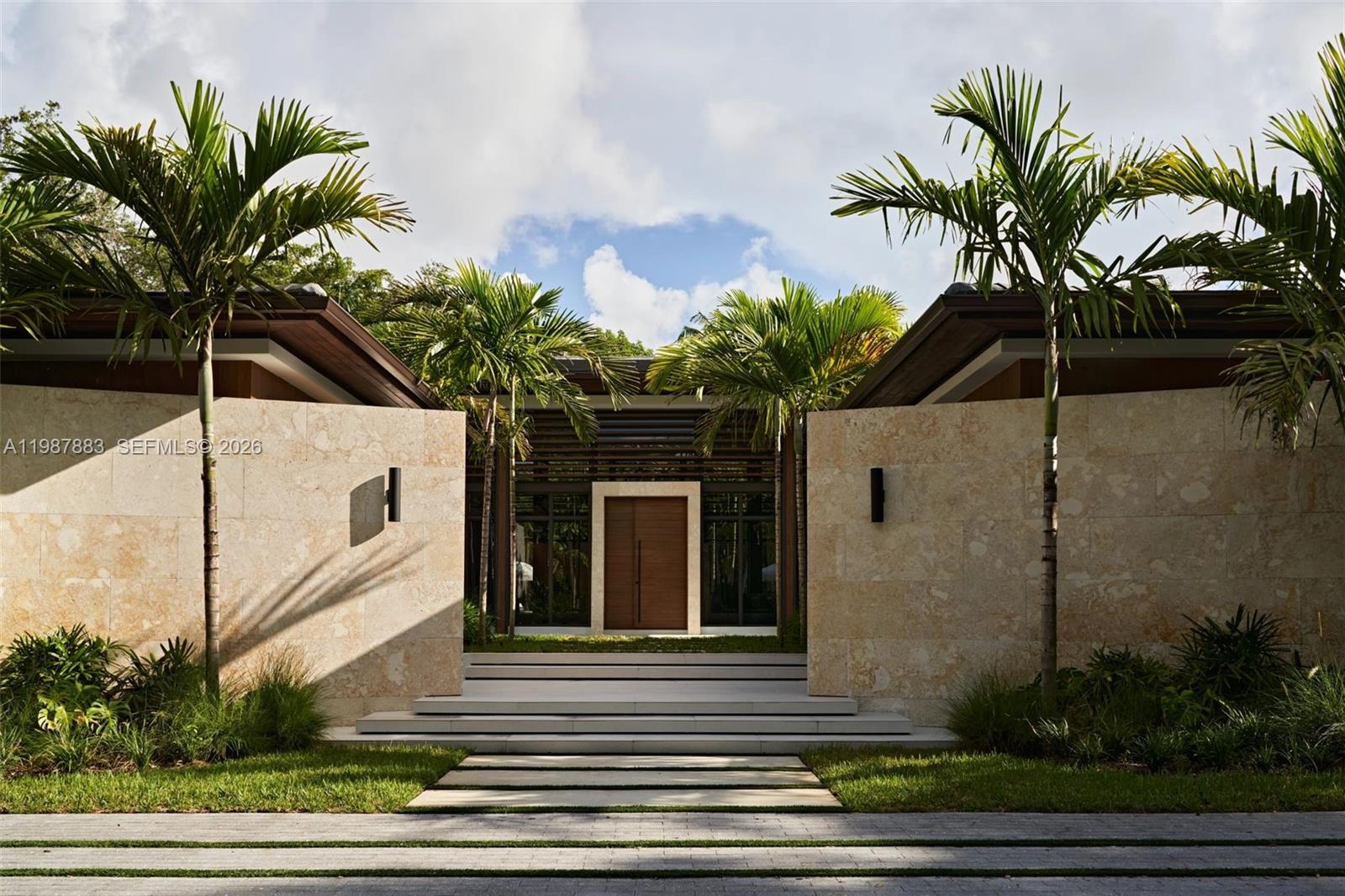 A modern home entrance features a wooden door, stone walls, and palm trees — 6371 SW 107th St, Pinecrest FL 33156, PINECREST, FL