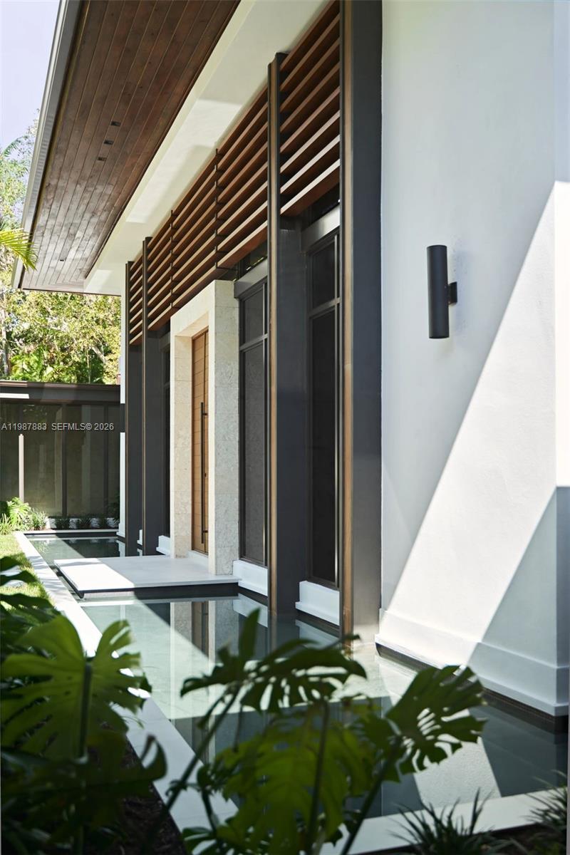 A modern home entrance features a wooden door, slatted wood accents, and a reflecting pool — 6371 SW 107th St, Pinecrest FL 33156, PINECREST, FL