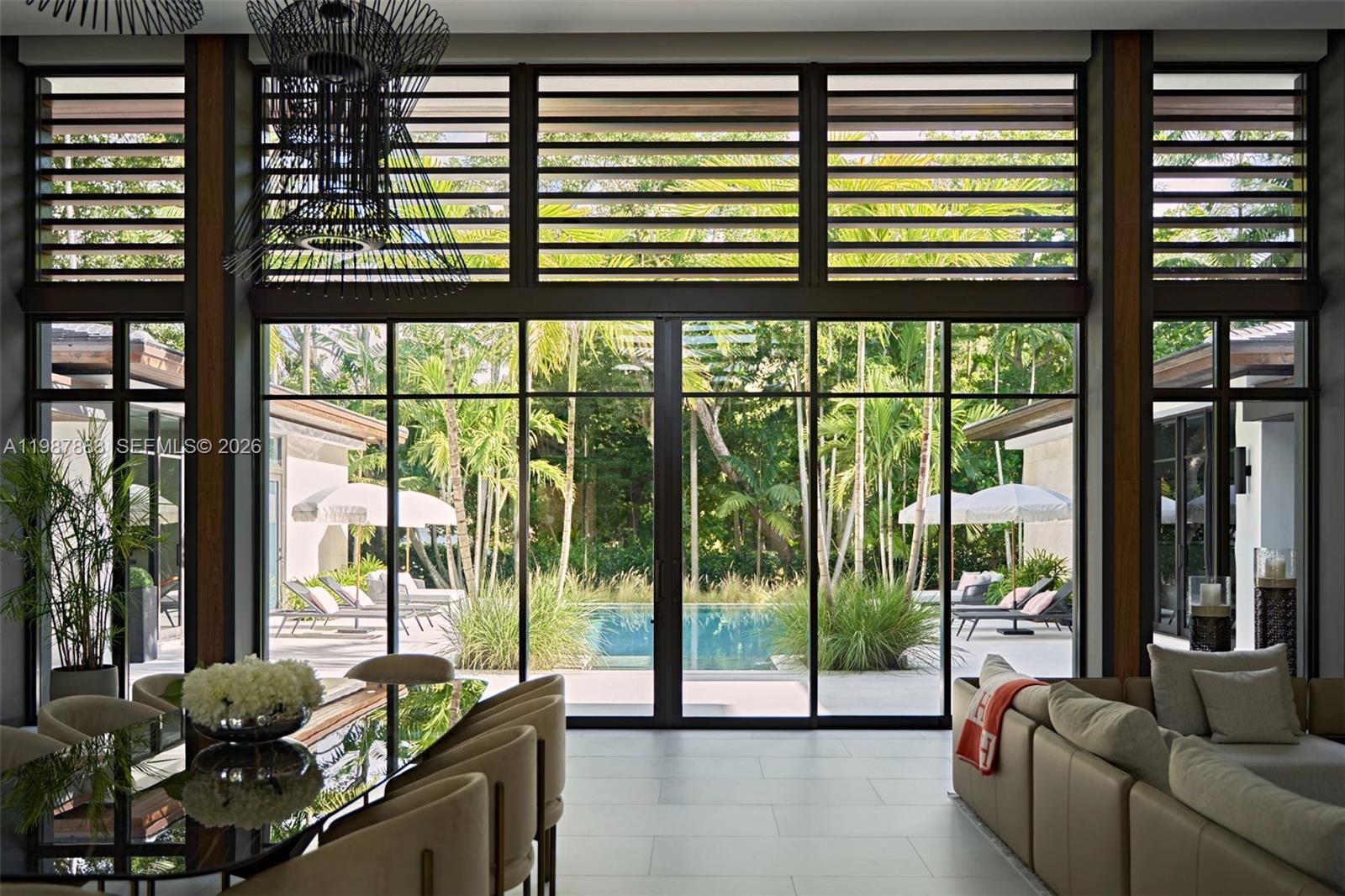 A dining and living area features floor-to-ceiling windows overlooking a pool and tropical landscaping — 6371 SW 107th St, Pinecrest FL 33156, PINECREST, FL