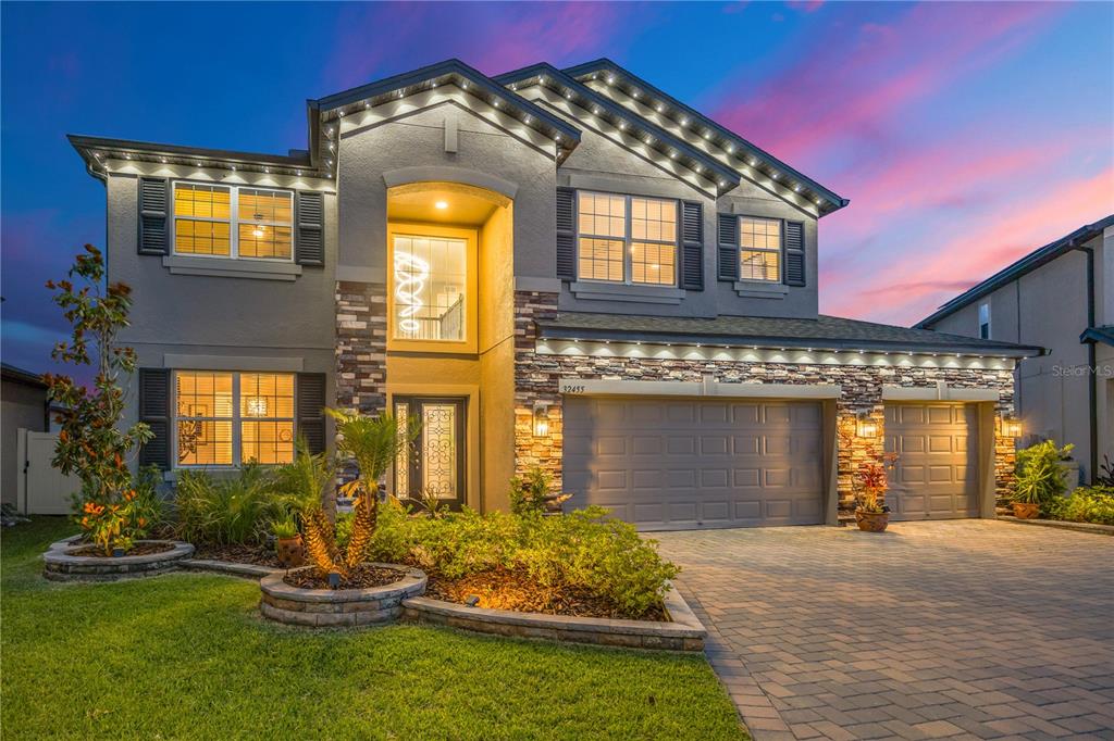 A two-story house with a stone facade, a three-car garage, and exterior accent lighting — 32455 SAPNA CHIME DRIVE, WESLEY CHAPEL, FL