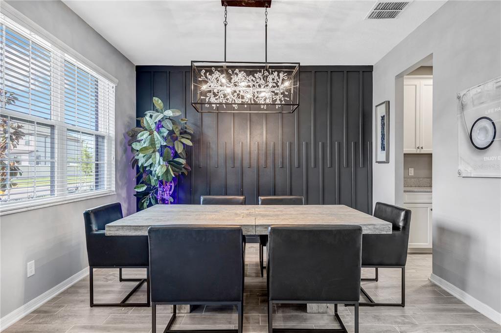 A dining room features a rustic wooden table, black chairs, and a dark paneled accent wall — 32455 SAPNA CHIME DRIVE, WESLEY CHAPEL, FL