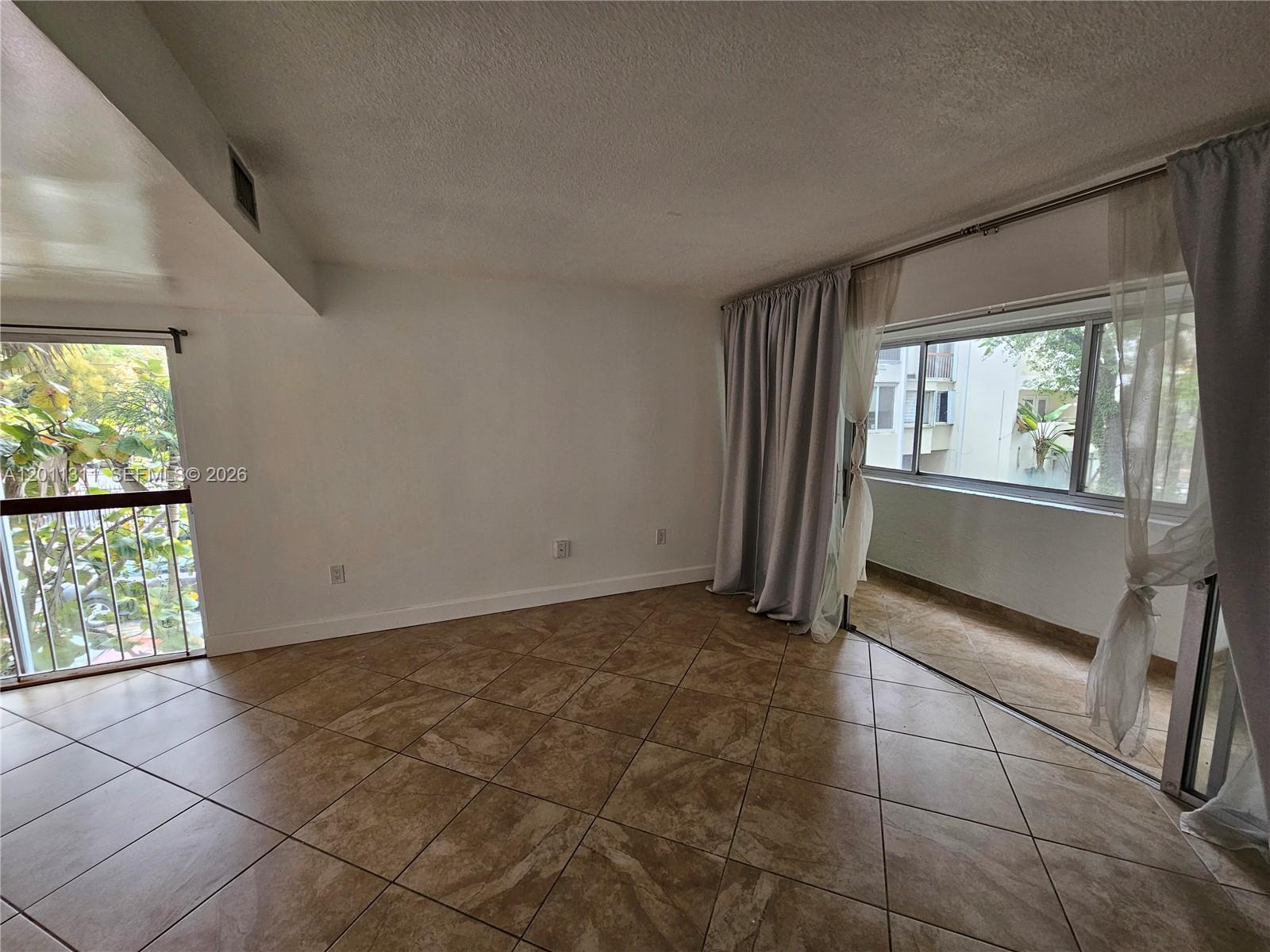 An empty room features beige tile flooring, white walls, and sliding glass doors to a balcony — 1912 SW 17th Ave # 11, Miami FL 33145, MIAMI, FL