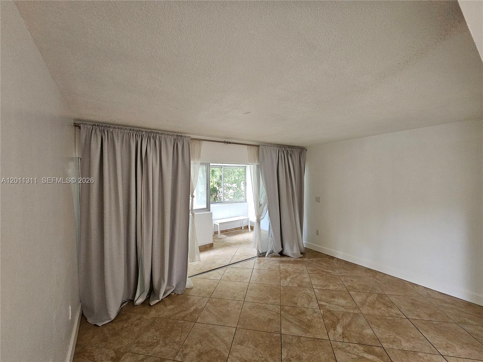 A room with beige tile flooring, white walls, and sliding glass doors leading to a balcony — 1912 SW 17th Ave # 11, Miami FL 33145, MIAMI, FL