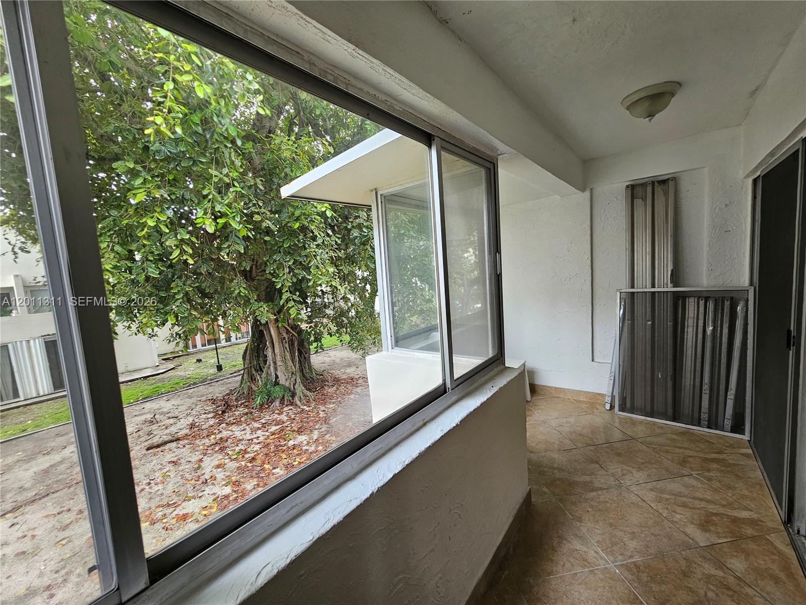 A tiled balcony overlooks a large tree through a windowed enclosure — 1912 SW 17th Ave # 11, Miami FL 33145, MIAMI, FL
