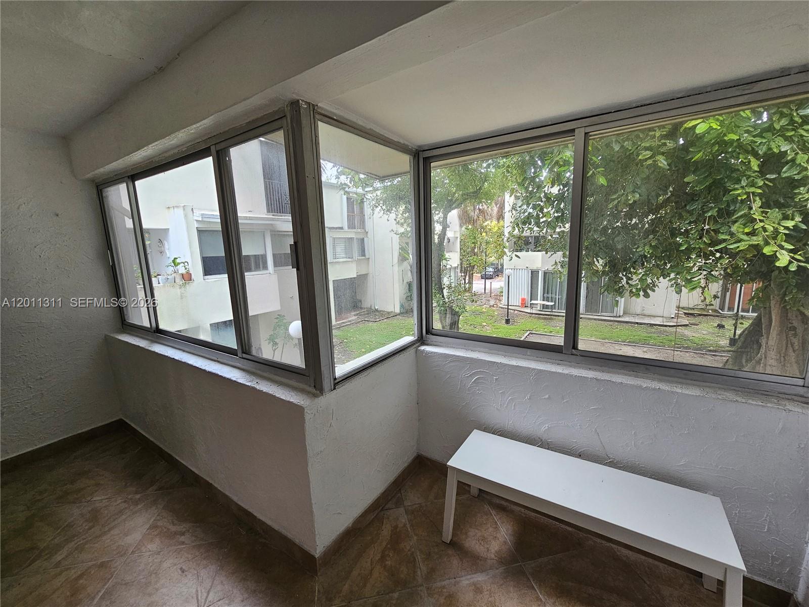 A sunroom features tile flooring, white textured walls, and large windows overlooking a courtyard — 1912 SW 17th Ave # 11, Miami FL 33145, MIAMI, FL