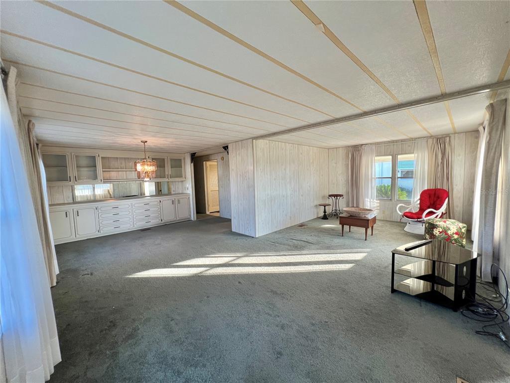 A living room features light wood-paneled walls, green carpeting, built-in cabinetry, and a red chair — 180 HIBISCUS WAY, LEESBURG, FL