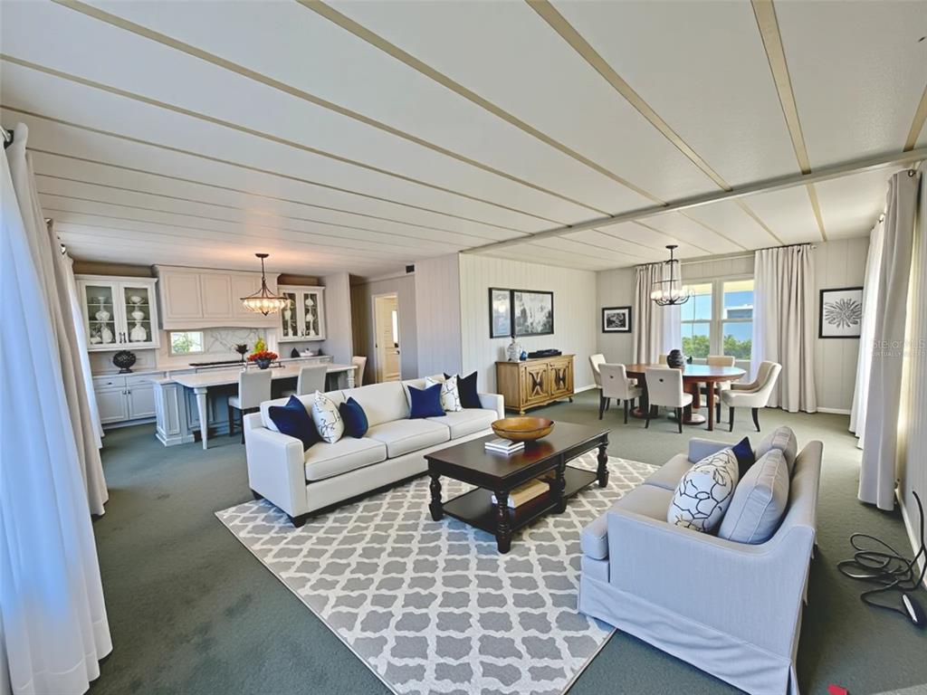 An open-concept living room, dining area, and kitchen with light-colored furniture and green carpeting — 180 HIBISCUS WAY, LEESBURG, FL