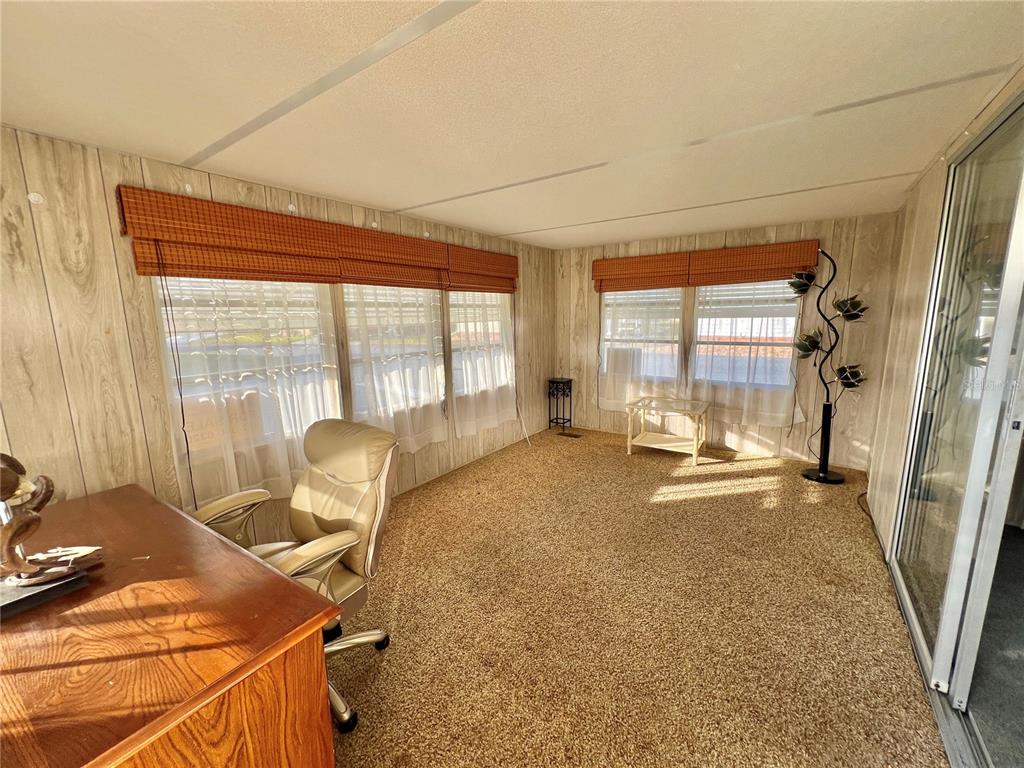 A sunroom features wood-paneled walls, tan carpeting, large windows with orange shades, and a desk — 180 HIBISCUS WAY, LEESBURG, FL