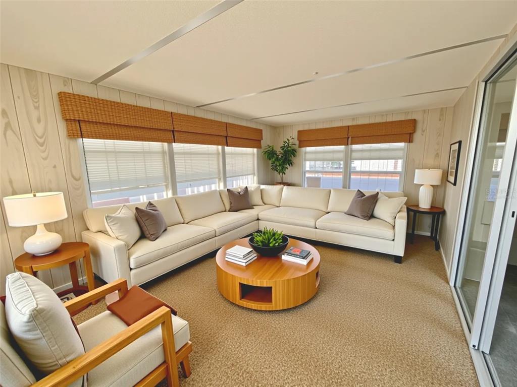 A sunroom features a large sectional sofa, a round wooden coffee table, and wood-paneled walls — 180 HIBISCUS WAY, LEESBURG, FL