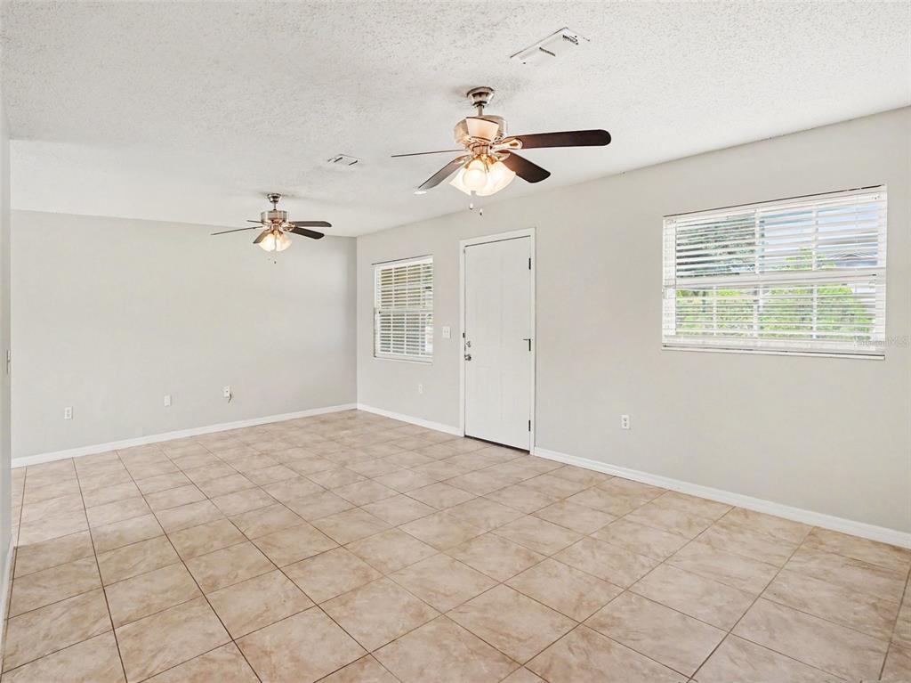 An empty room with tiled floors, two ceiling fans, a white door, and two windows — 3255 KELVINGTON DRIVE, ORLANDO, FL