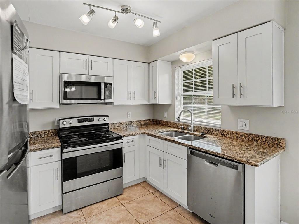 A kitchen features white cabinets, granite countertops, stainless steel appliances, and tile flooring — 3255 KELVINGTON DRIVE, ORLANDO, FL