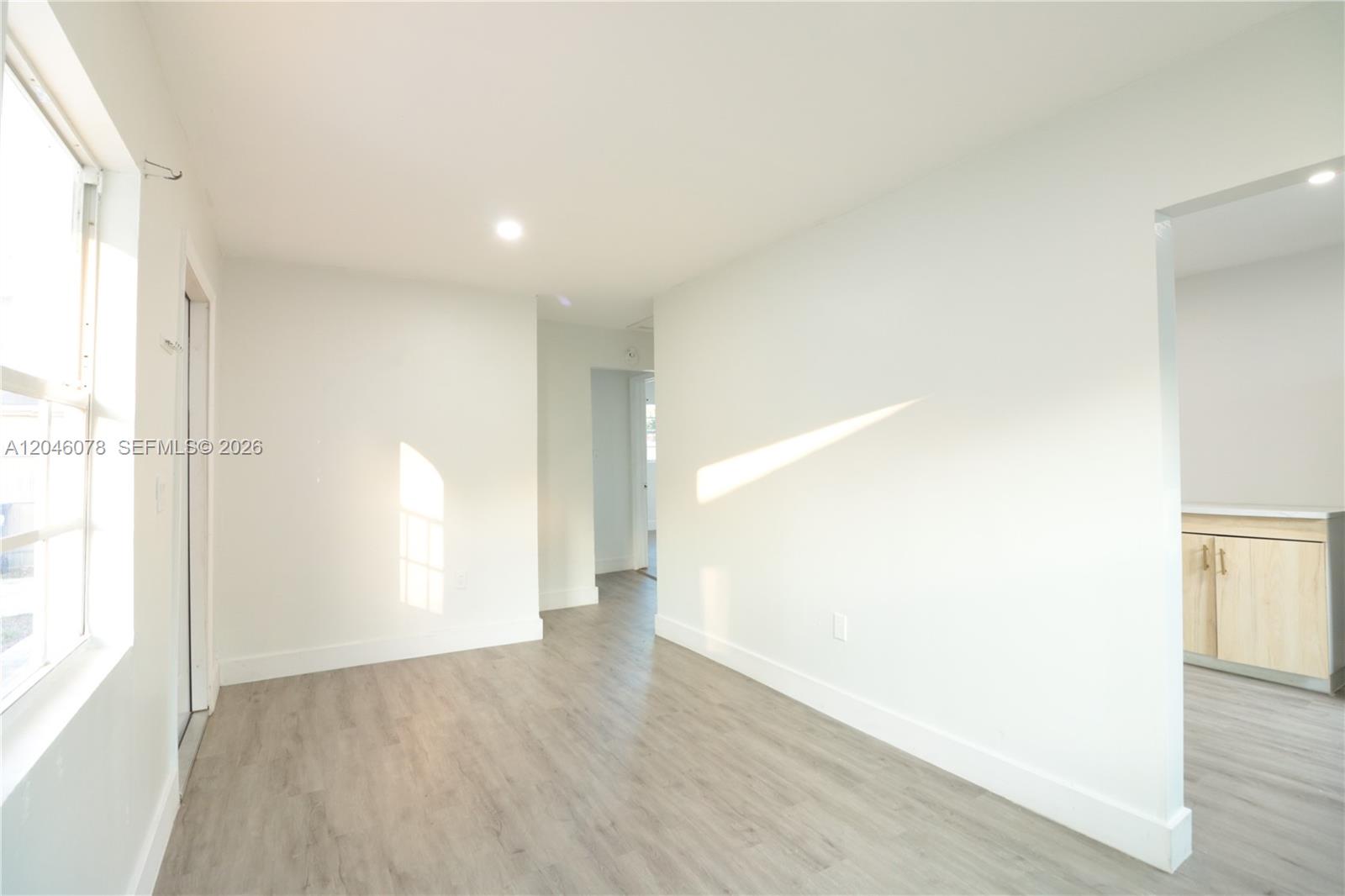 A bright, empty room features light wood-look flooring, white walls, and a doorway to a kitchen — 1768 NW 112th Ter # 1, Miami FL 33167, MIAMI, FL