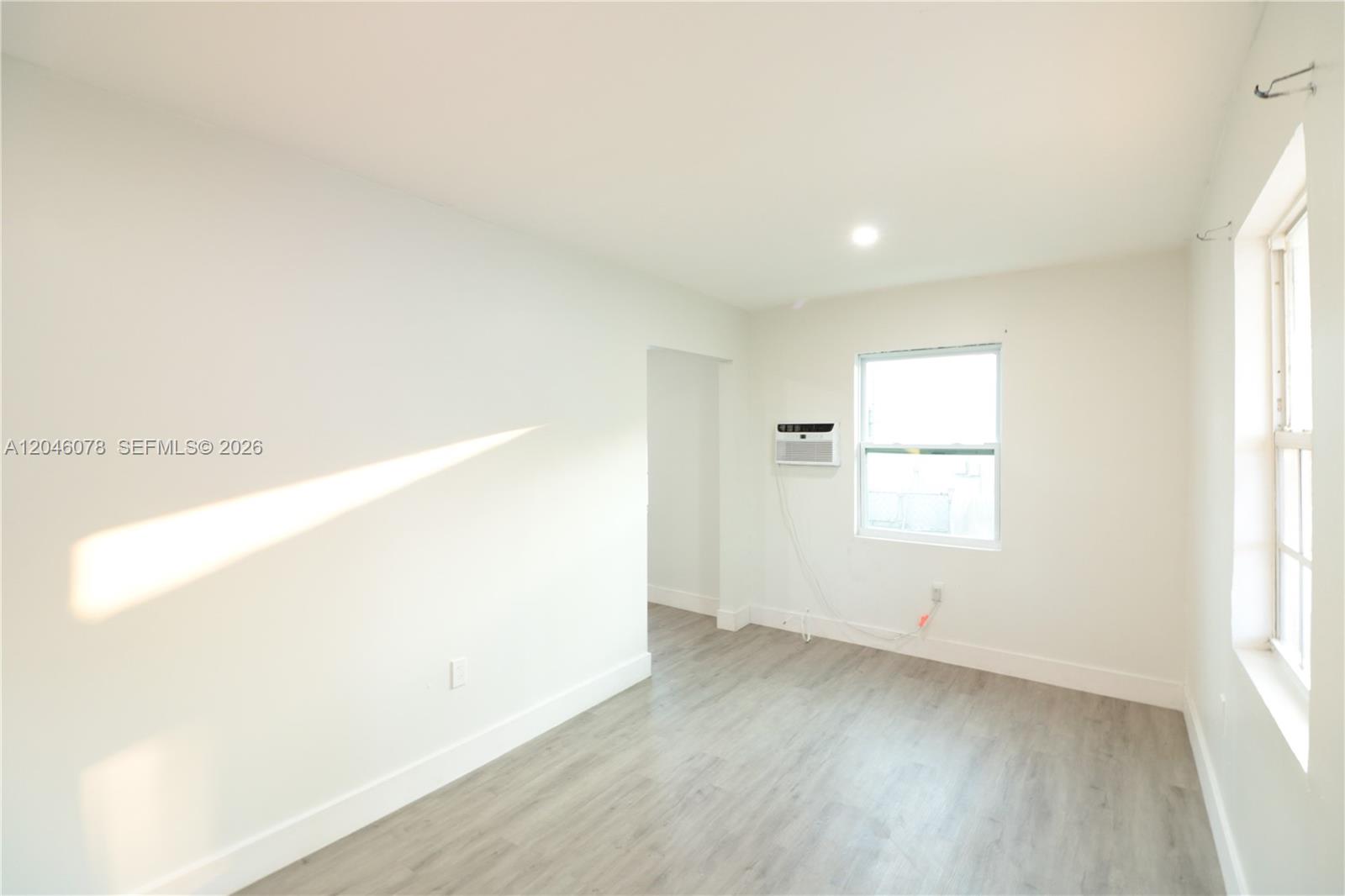 A bright, empty room features white walls, light wood-look flooring, and a window air conditioner — 1768 NW 112th Ter # 1, Miami FL 33167, MIAMI, FL