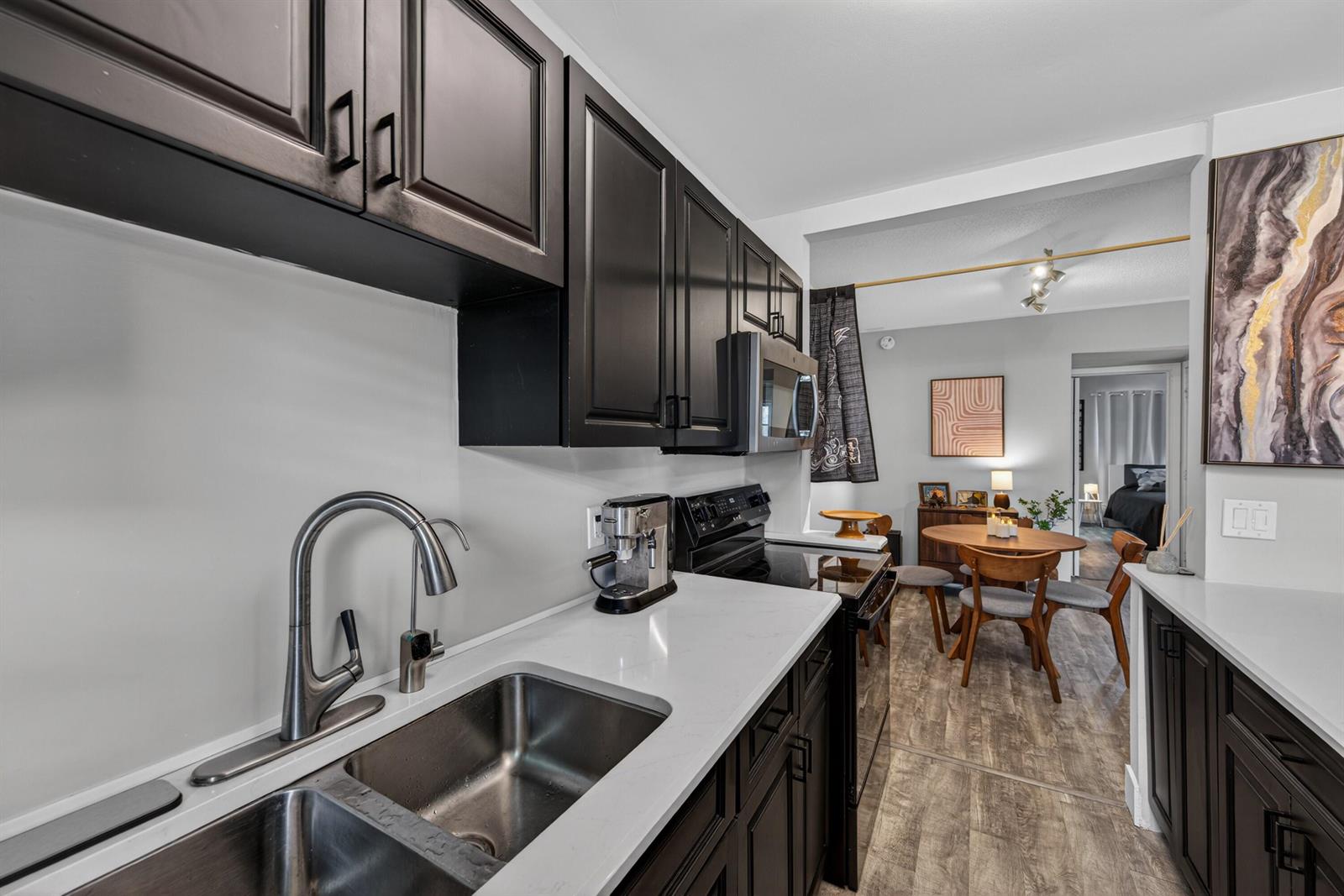 A kitchen with dark cabinets, white countertops, and a stainless steel sink leads to a dining area — 2110 NE 42nd Street # 4b, Lighthouse Point FL 33064, LIGHTHOUSE POINT, FL