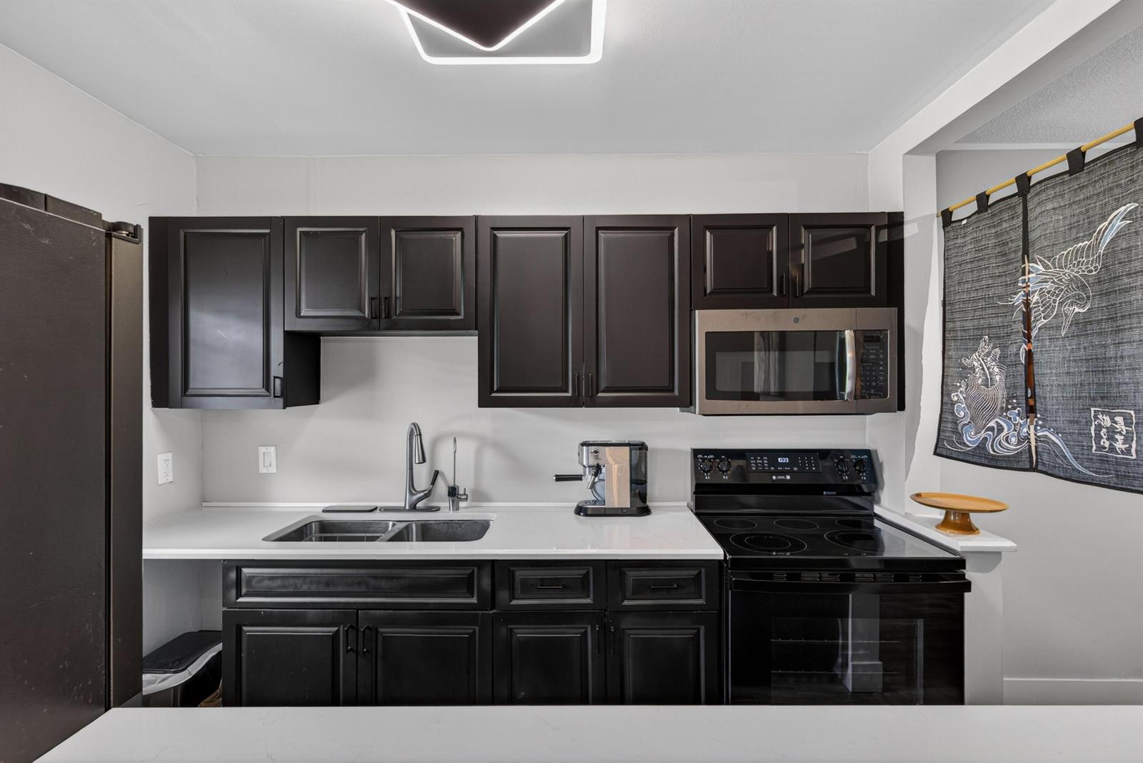 A kitchen features dark cabinets, white countertops, stainless steel appliances, and a decorative wall hanging — 2110 NE 42nd Street # 4b, Lighthouse Point FL 33064, LIGHTHOUSE POINT, FL