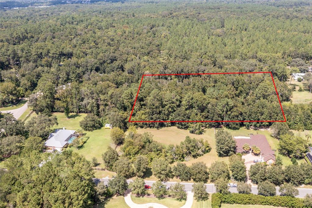 An aerial view shows a wooded lot outlined in red situated between two residential homes — 10971 SW 8TH AVENUE, GAINESVILLE, FL