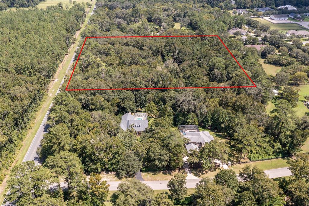 An aerial view shows a large, rectangular wooded lot outlined in red behind two houses — 10971 SW 8TH AVENUE, GAINESVILLE, FL