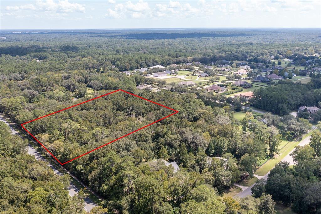 An aerial view shows a rectangular plot of land outlined in red amidst dense trees — 10971 SW 8TH AVENUE, GAINESVILLE, FL