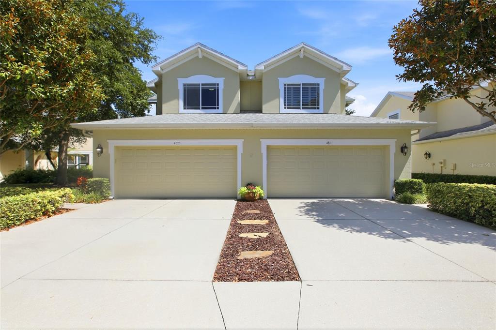 A two-story duplex features two beige garage doors and a central stone walkway — 477 HARBOR RIDGE DRIVE, PALM HARBOR, FL