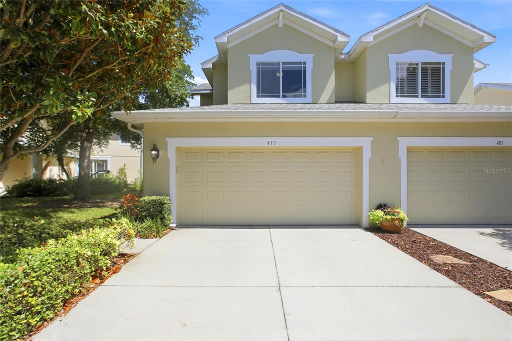 A two-story townhouse exterior features a beige stucco facade, a two-car garage, and a driveway — 477 HARBOR RIDGE DRIVE, PALM HARBOR, FL