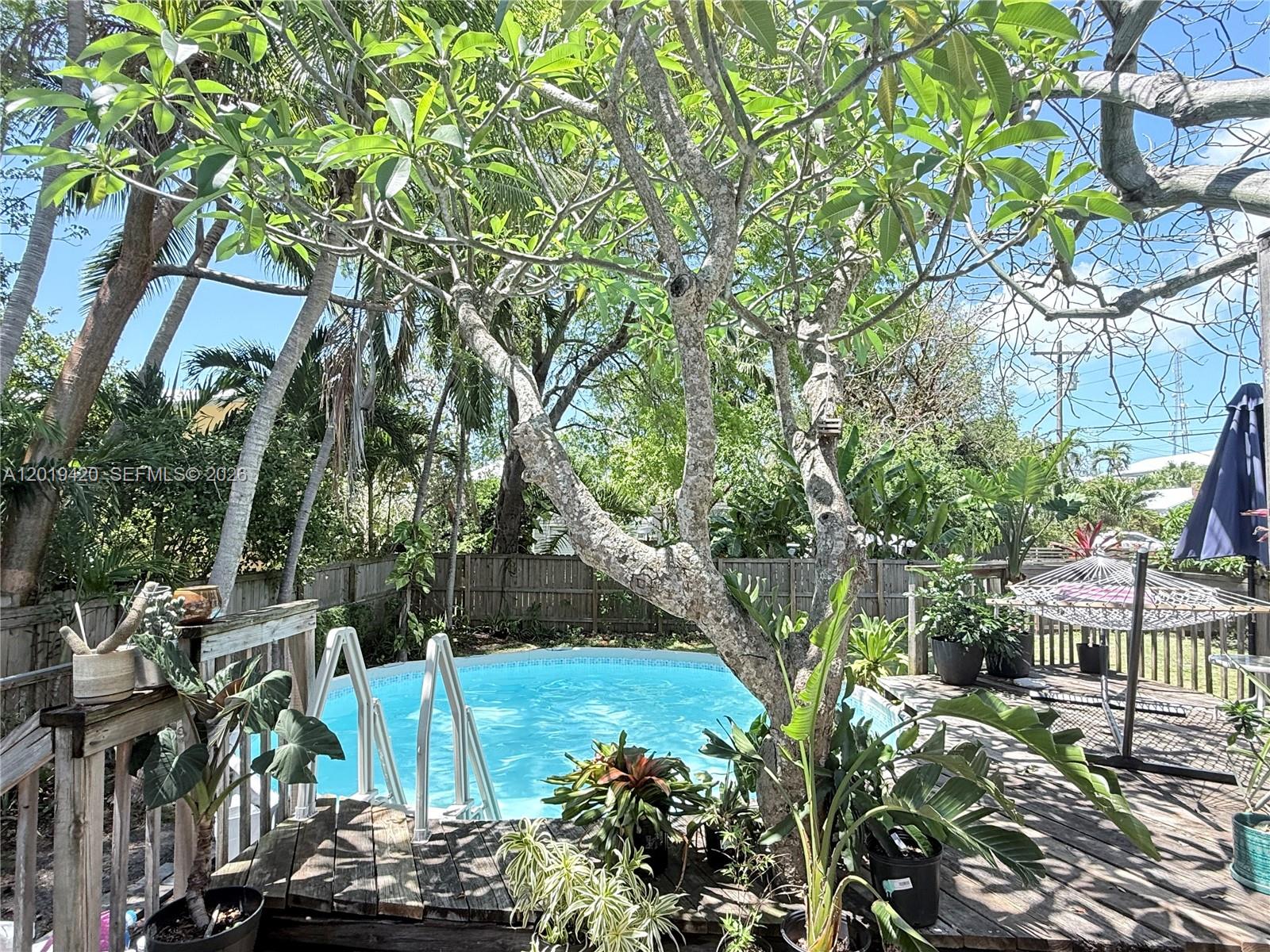 A backyard features a wooden deck, an above-ground swimming pool, and various potted plants — TAVERNIER, FL