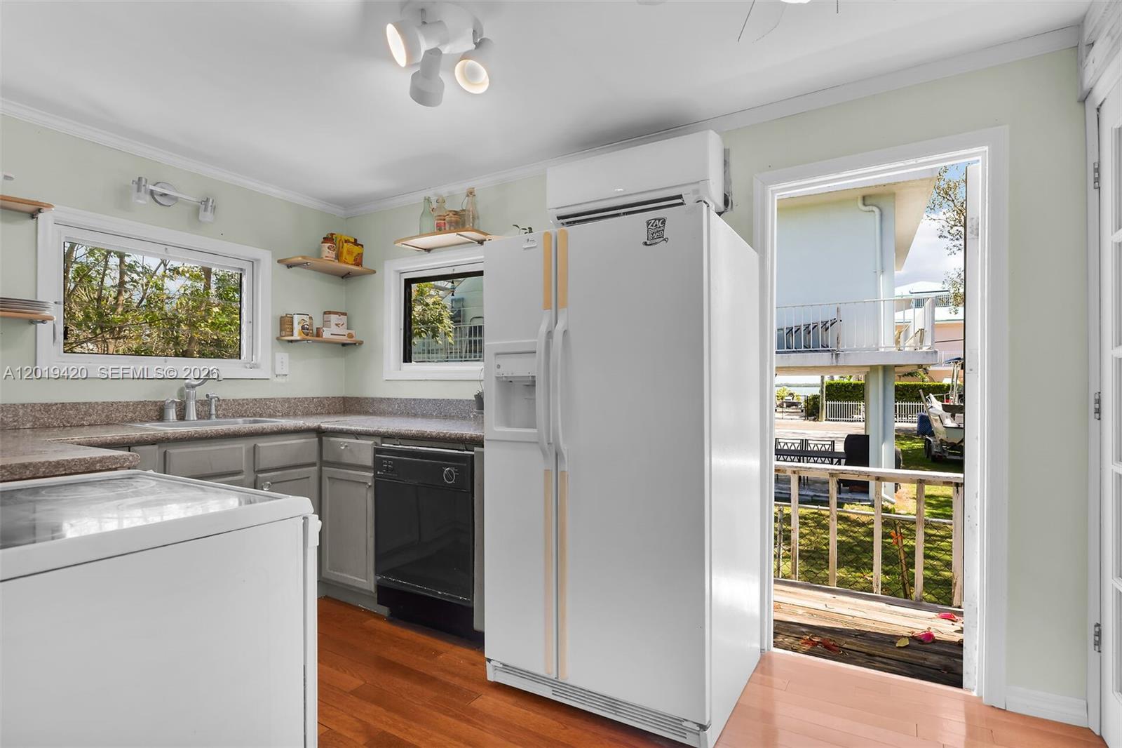 A kitchen features gray cabinets, granite countertops, a white refrigerator, and a door to a deck — TAVERNIER, FL