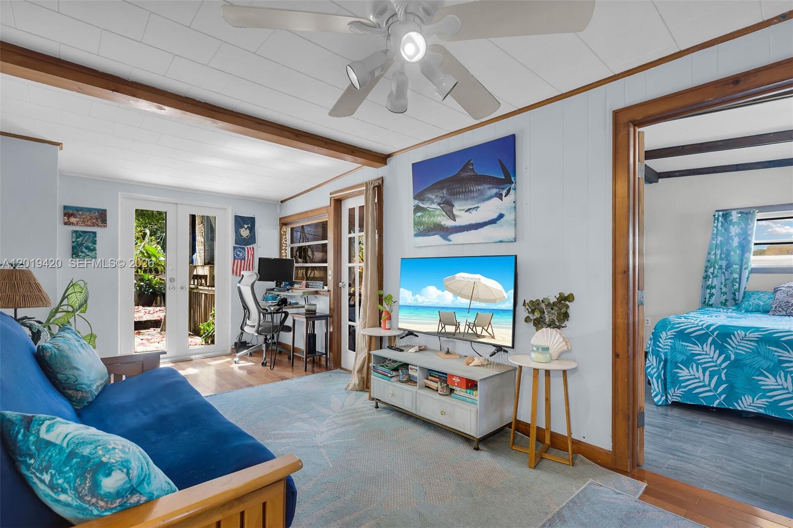 A living room features a blue sofa, a television, and a doorway to a bedroom — TAVERNIER, FL