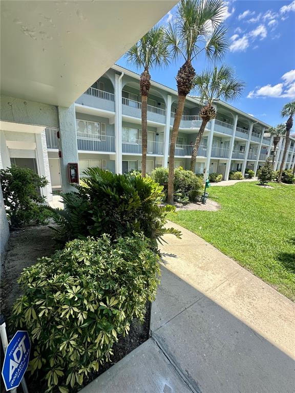A multi-story apartment building features balconies, palm trees, and a sidewalk on a sunny day — 115 OYSTER BAY CIRCLE UNIT 170, ALTAMONTE SPRINGS, FL