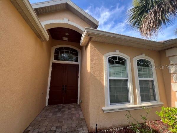 The exterior of a house features a tan stucco facade, double front doors, and windows — 8913 SW 74TH AVENUE, GAINESVILLE, FL